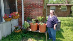 Sarah standing near a picnic table with pots on it and hanging baskets nearby